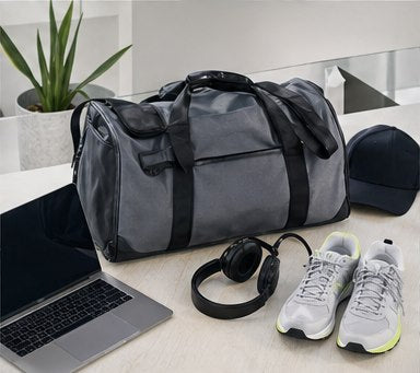 Sporttasche mit Alltagsequipment auf hellem Schreibtisch